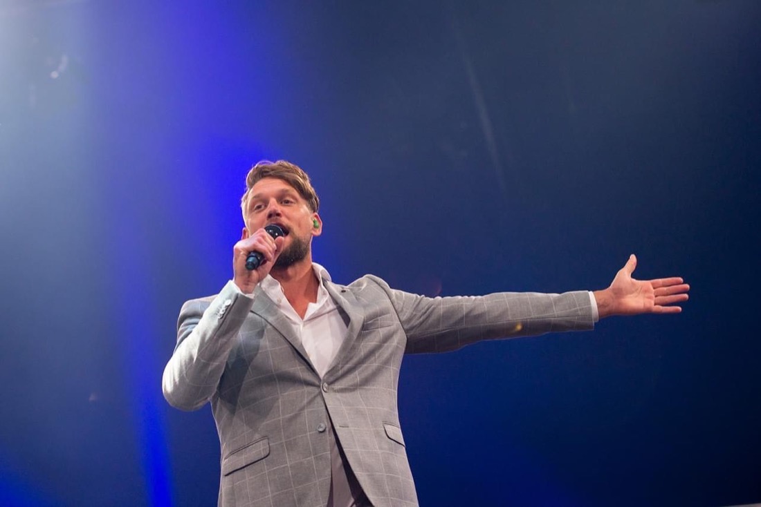Marcel Swerissen zingt met een microfoon in zijn hand en zijn arm gestrekt naar de zaal.